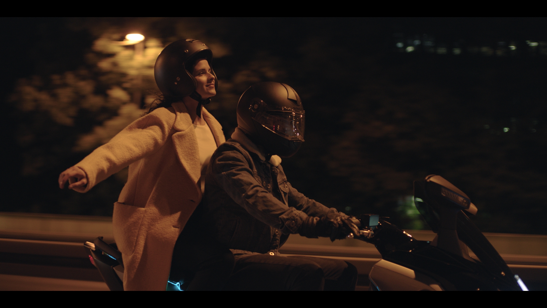 Zwei Menschen auf einem Motorroller bei Nacht.